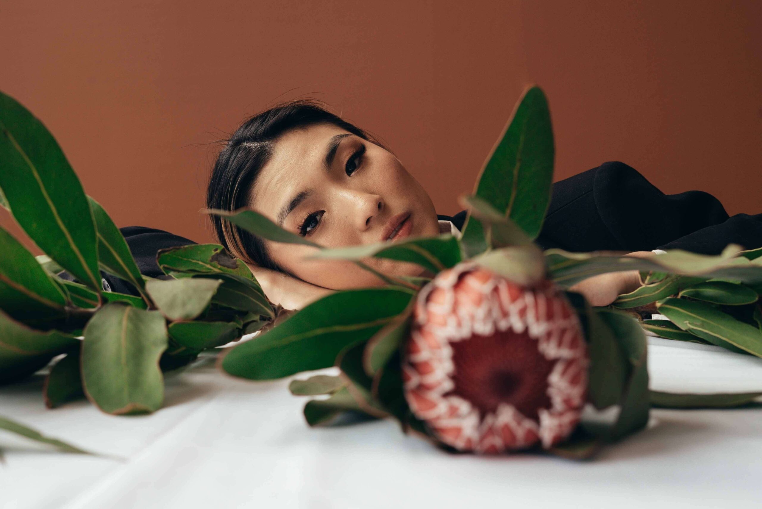 Woman laying her head on table behind a flower.